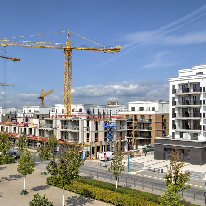 Ein Neubaugebiet mit Wohngebäuden, im Hintergrund sind Baukräne und eine Baustelle zu sehen.