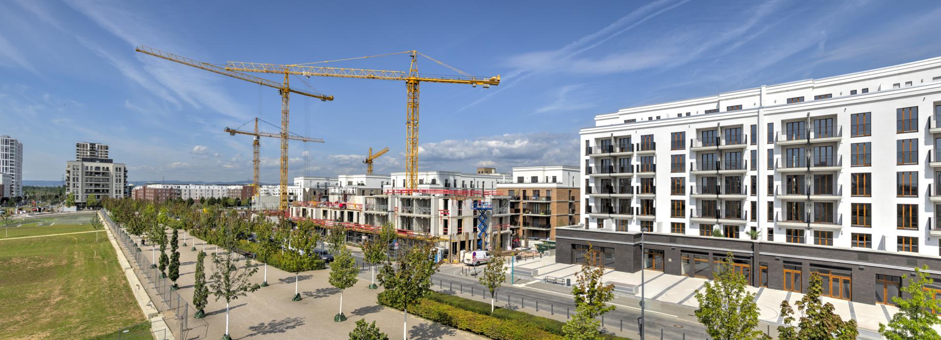 Ein Neubaugebiet mit Wohngebäuden, im Hintergrund sind Baukräne und eine Baustelle zu sehen.